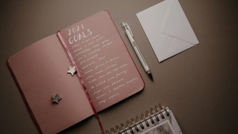 A flat lay image of an open journal with 2021 goals, pen, and envelope on a brown background.