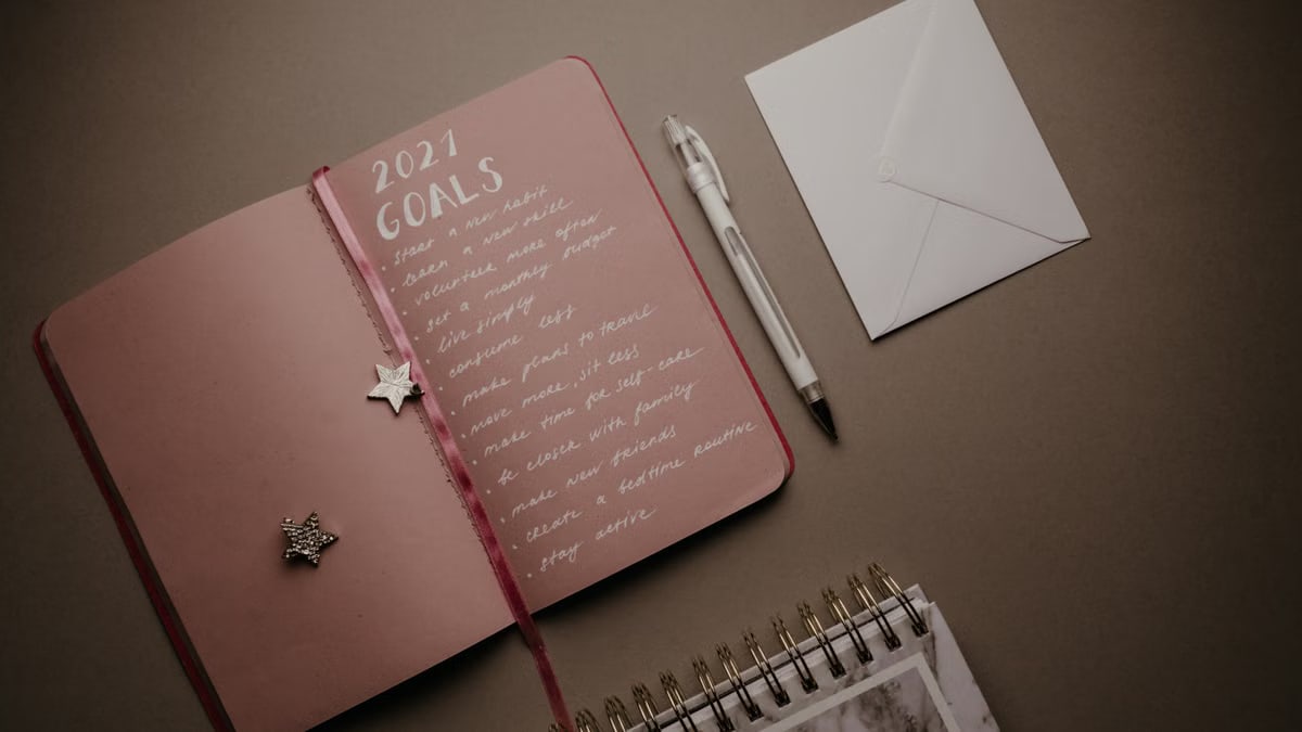A flat lay image of an open journal with 2021 goals, pen, and envelope on a brown background.